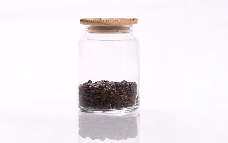 May include: A clear glass jar with a wooden lid filled with dark brown coffee beans.