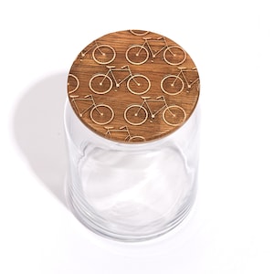 May include: A clear glass jar with a wooden lid. The lid is decorated with a repeating pattern of bicycles.
