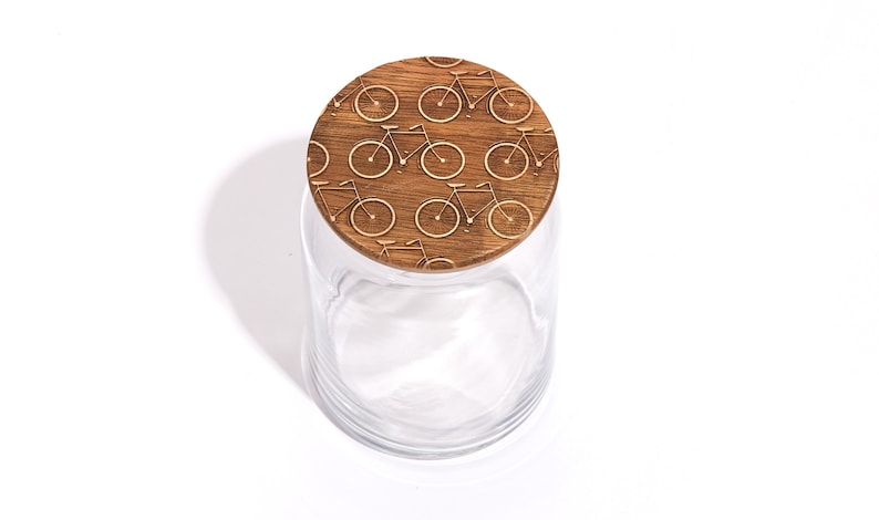 May include: A clear glass jar with a wooden lid. The lid is decorated with a repeating pattern of bicycles.