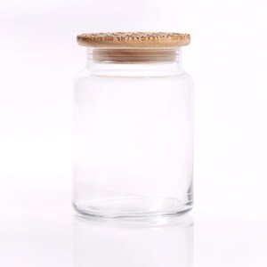May include: A clear glass jar with a wooden lid. The jar is empty and has a smooth, rounded shape.