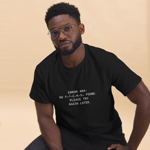 Puede incluir: Camiseta negra con texto blanco: "ERROR 404: NO F-*-C-K-S- FOUND. PLEASE TRY AGAIN LATER." La camiseta es de cuello redondo.