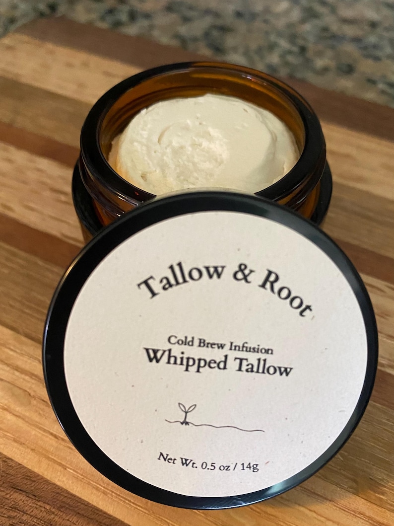 May include: An open amber glass jar filled with a creamy, off-white whipped tallow product. The lid, with the text "Tallow & Root" and "Whipped Tallow", is next to the jar. The net weight is 0.5 oz / 14g.