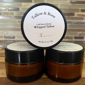 May include: Three small jars of whipped tallow with black lids and brown glass. The labels read "Tallow & Root" and "Whipped Tallow." Each jar contains 0.5 oz / 14g of product. The jars are arranged on a wooden surface.