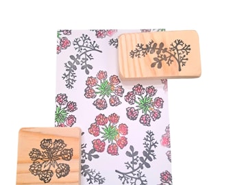 May include: Wooden stamps with floral designs and a printed floral pattern on white paper. The stamps are rectangular and square, with black ink floral patterns. The paper has a repeating pattern of red and green flowers and gray leaves. The text "@lapirose_stamp" is in the bottom right corner.