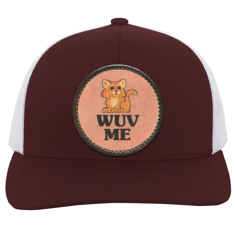 May include: A burgundy trucker hat with a white mesh back. The front features a circular patch with a cartoon cat and the words "WUV ME" in a bold font. The hat has a curved brim and a button on top.