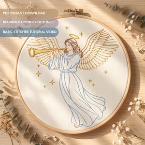 May include: An embroidery hoop containing white fabric with a stitched design of an angel playing a golden trumpet. The angel has large wings, a halo, and a flowing gown outlined in blue thread. Small golden stars surround the figure.