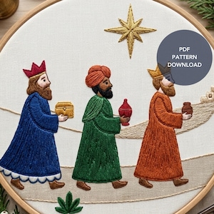 May include: An embroidery hoop containing a fabric panel with a stitched scene of three figures in robes walking toward a distant building. Above them is a gold star. The figures carry a gold chest, a red vessel, and a brown jar. Text reads PDF PATTERN DOWNLOAD.