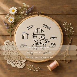 May include: A wooden embroidery hoop with a canvas featuring a construction worker illustration, the words "BUILD" and "CREATE", and other construction-related icons. The image includes flowers, lace, scissors, and thread on a wooden surface.