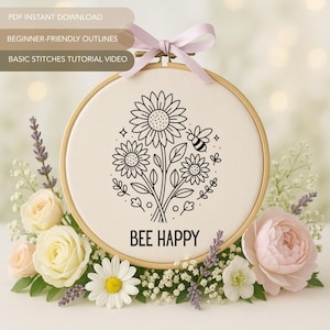 Op de afbeelding: Een borduurring met een bloemenontwerp van zonnebloemen en een bij, met de woorden "BEE HAPPY". Het ontwerp is in zwart en wit. De ring is omgeven door bloemen en groen, met een roze lint. Tekst bovenaan luidt "PDF INSTANT DOWNLOAD, BEGINNER-FRIENDLY OUTLINES, BASIC STITCHES TUTORIAL VIDEO."