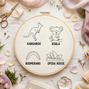 May include: An embroidery hoop with a kangaroo, koala, boomerang, and Opera House design. The words "Kangaroo", "Koala", "Boomerang", and "Opera House" are printed below each image. The hoop is surrounded by flowers, lace, and sewing supplies.