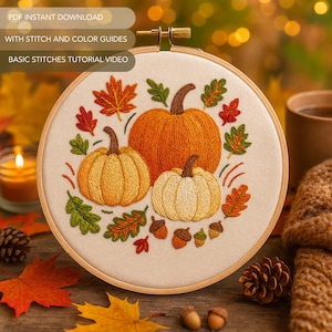 Op de afbeelding: Een ronde borduurring met een herfstthema. Het ontwerp toont drie geborduurde pompoenen in oranje en geel, omringd door herfstbladeren en eikels. De tekst "PDF INSTANT DOWNLOAD", "WITH STITCH AND COLOR GUIDES" en "BASIC STITCHES TUTORIAL VIDEO" is zichtbaar.