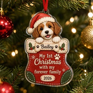 May include: A clear acrylic Christmas ornament shaped like a stocking featuring a brown and white puppy wearing a red Santa hat. The stocking displays the name Bailey, the text My 1st Christmas with my forever family, and the year 2026.