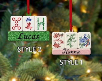 May include: Two personalized Christmas ornaments. One has green glitter with the name "Lucas" and three tiles. The other has pink glitter with the name "Hanna" and three tiles. Each ornament has a red ribbon for hanging.