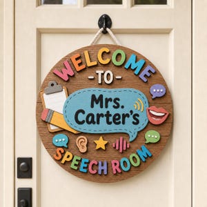 Puede incluir: Un letrero redondo de madera con acabado de veta de madera que presenta el texto "WELCOME TO" y "SPEECH ROOM" en letras 3D coloridas. Un globo de texto azul central muestra "Mrs. Carter's" con iconos de portapapeles, lápiz, oreja, estrella y boca.