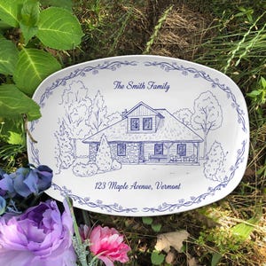 Op de afbeelding: Witte ovale schaal met een blauwe illustratie van een huis, bomen en een bloemenrand. De tekst luidt "The Smith Family" en "123 Maple Avenue, Vermont". Het ontwerp doet denken aan een handgetekende schets.