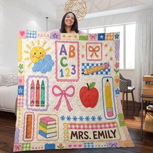 May include: A quilted blanket featuring a cream background with colourful school-themed illustrations including a yellow sun, alphabet letters, numbers, a pencil, crayons, a red apple, books, and a pink bow. The text MRS. EMILY is printed at the bottom.