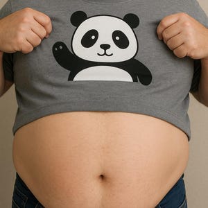 Puede incluir: Camiseta gris con un oso panda de dibujos animados en blanco y negro. El panda está saludando. La persona lleva vaqueros azules.