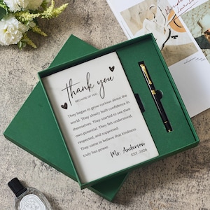 May include: A dark green gift box containing a white rectangular card with the text Thank you BECAUSE OF YOU followed by a paragraph about kindness and Mr. Anderson EST. 2026, accompanied by a black and gold pen nestled in a custom cutout.