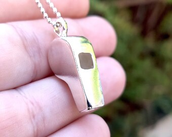 May include: A silver whistle pendant necklace. The whistle is a classic design with a rectangular opening.
