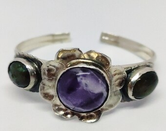 May include: A silver bracelet with a flower design featuring a purple amethyst stone and two green stones.