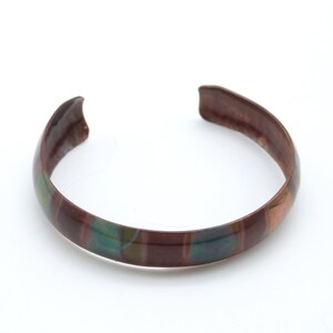 May include: A copper bracelet with a multi-colored enamel design. The enamel is in shades of brown, green, and blue.