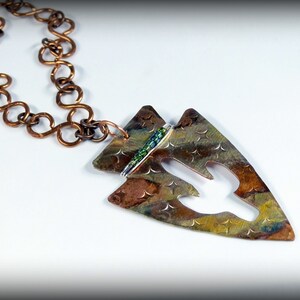 May include: A copper arrowhead pendant necklace with a green and silver bead accent. The pendant is textured and has a cutout design. The necklace is made of a copper chain.