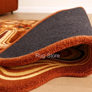 May include: A rolled-up area rug with a brown and yellow abstract pattern. The rug has a dark gray backing and a rust-colored border. The text "Rug Store" is visible on the edge of the rug.