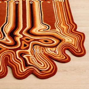 May include: A unique, abstract rug with a flowing, organic design. The rug features a palette of warm colors, including shades of brown, orange, and cream, with black accents. The edges have a wavy, irregular shape. The text "Rug Store" is visible.