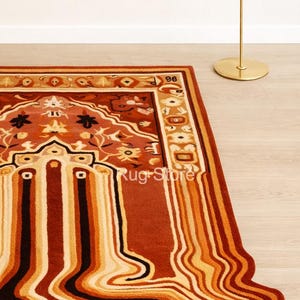 May include: A rectangular rug with a unique design featuring a mix of warm colors. The rug has a central pattern with floral and geometric elements in shades of red, orange, and beige. The border is a darker red, and the edge has a wavy, melted appearance.