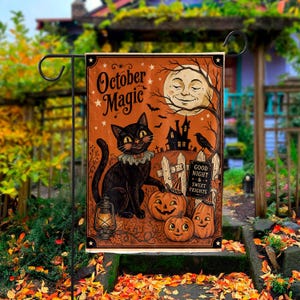 May include: A rectangular garden flag with an orange background featuring a black cat, a lantern, two jack-o'-lanterns, a moon with a face, and a haunted house. The text reads October Magic and Good Night Sweet Frights in black lettering.