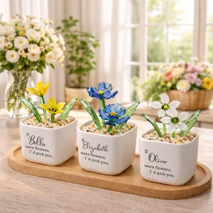 May include: Three white square ceramic pots with glass flowers, each with a different name and the text "If [name] were flowers, I'd pick you." The flowers are yellow, blue, and white, with green glass stems and leaves. The pots sit on a wooden tray.