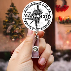 May include: A round, white badge with the text "MAN OF GOD" and a sword graphic. The badge also includes Bible verses from Isaiah and Ephesians. The badge is attached to a clear plastic retractable badge holder.