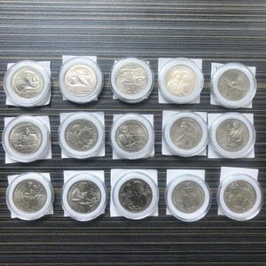 May include: A collection of fifteen silver coins, each encased in a clear plastic holder and mounted on a white card. The coins feature various designs and portraits, likely commemorative or collectible pieces. The arrangement is neat, suggesting a display or storage setup.