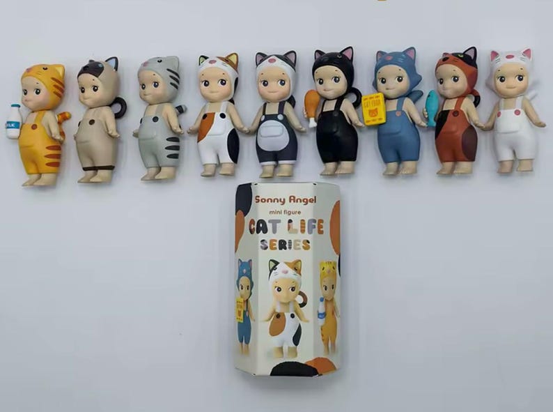May include: A selection of Sonny Angel mini figures from the Cat Life Series. The figures are dressed in cat-themed outfits, with various colours and accessories. The packaging box is also visible, featuring the series name and illustrations.