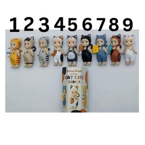 May include: A display of nine Sonny Angel mini figures from the Cat Life Series. Each figure is a small, stylised doll with cat-themed outfits and accessories. The figures are arranged in a row, with a box featuring the series' branding.