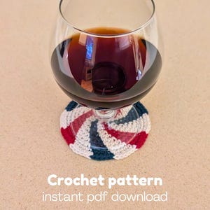 May include: A glass of red wine sits on a handmade crochet coaster. The coaster has a spiral design with red, white, and blue stripes. The image includes the text "Crochet pattern instant pdf download."