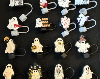 Può includere: Una collezione di ciondoli a tema Halloween con disegni di fantasmi bianchi con vari accessori e testo. Alcuni ciondoli presentano frasi come "STRAIGHT GHOSTED", "BOO" e "OH SHEET". Ogni ciondolo ha una base nera e un cinturino bianco.