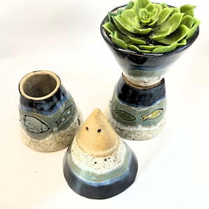 Op de afbeelding: Een keramische zout- en pepermolenset en een decoratieve vaas met een vetplant. De set bevat een kegelvormige zoutstrooier en een cilindrische pepermolen, beide met visontwerpen. De vaas heeft een gelaagd ontwerp met vismotieven.