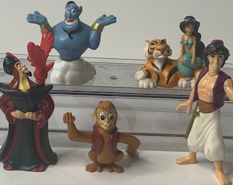 May include: A set of six plastic Disney Aladdin figures, including Aladdin, Jasmine, Genie, Abu, Jafar, and Rajah. The figures are in a clear plastic container.