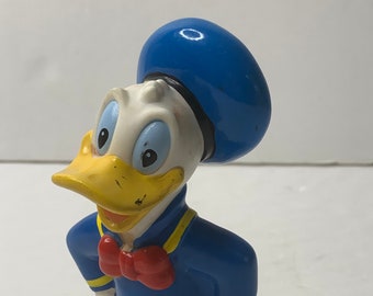 Puede incluir: Una figurita de plástico amarilla y azul de Donald Duck con un sombrero de marinero azul y una pajarita roja.