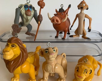 May include: A set of six The Lion King character ornaments. The ornaments are made of plastic and feature Simba, Nala, Mufasa, Pumbaa, Timon, and Rafiki. The ornaments are all in their signature colors and have a loop for hanging.