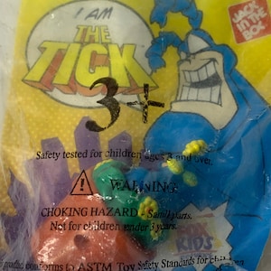 May include: A blue and yellow plastic toy of The Tick, a superhero character from the comic book series. The toy is packaged in a clear plastic bag with a warning label that says "Choking Hazard - Small parts. Not for children under 3 years."