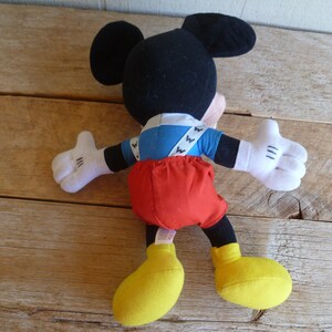 Może przedstawiać: Pluszowa zabawka Mickey Mouse ubrana w niebiesko-białą koszulę, czerwone spodnie i ż&oacute;łte buty.