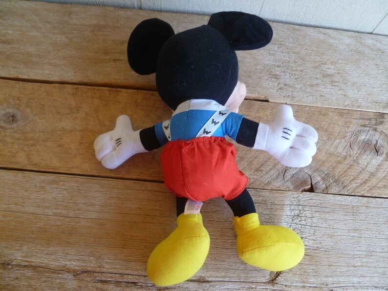 Może przedstawiać: Pluszowa zabawka Mickey Mouse ubrana w niebiesko-białą koszulę, czerwone spodnie i ż&oacute;łte buty.