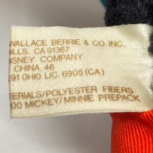 May include: A white tag with black text that reads "WALLACE BERRIE & CO. INC. ELLS, CA 91367 SNEY COMPANY CHINA, 46 291 OHIO LIC. 6905 (CA) ERIALS/POLYESTER FIBERS 00 MICKEY/MINNIE PREPACK"