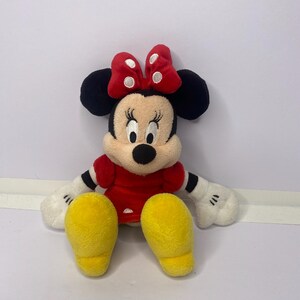 Pu&ograve; includere: Una bambola di peluche di Minnie Mouse, con un vestito rosso, scarpe gialle e un fiocco rosso a pois bianchi. La bambola ha orecchie nere, un naso nero e guanti bianchi. Il giocattolo &egrave; per bambini.