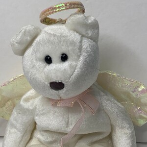 May include: White plush teddy bear with a pink ribbon and iridescent wings and halo. The bear is sitting with its wings spread out.