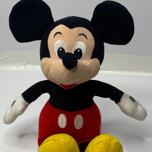 May include: A plush Mickey Mouse toy with black ears, a black body, red shorts with white buttons, and yellow shoes.