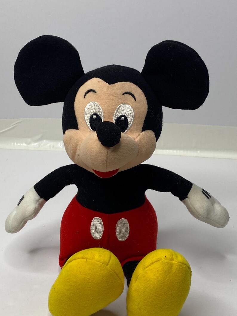 May include: A plush Mickey Mouse toy with black ears, a black body, red shorts with white buttons, and yellow shoes.