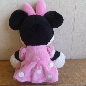Puede incluir: Un juguete de peluche rosa y negro de un rat&oacute;n de dibujos animados que lleva un vestido rosa con lunares blancos. El rat&oacute;n tiene un lazo rosa en la cabeza.